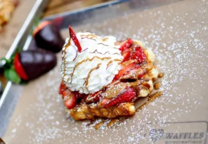 A Belgian waffle topped with strawberries, whipped cream, and caramel drizzle.