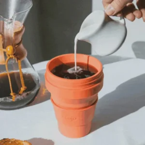 Pouring milk into coffee in an orange collapsible cup