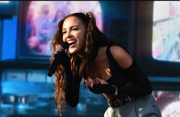 Lady rockstar performing on stage at a concert, holding a microphone in one hand, with vibrant lights illuminating the scene