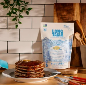 Stack of blue corn pancakes with syrup next to Long Table mix.